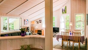 Interior acogedor de una cabaña con detalles de madera, una zona de comedor con mesa y sillas, y un espacio de estar con sofá y cojines.