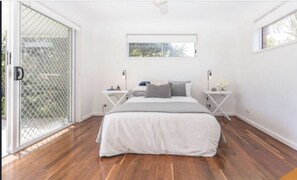 Relax in this serene bedroom with a large bed, two nightstands, and a sliding glass door leading to an outdoor area.