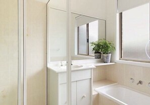 Bathroom features a white vanity with a mirror, sink, and cabinet, along with a bathtub and window.