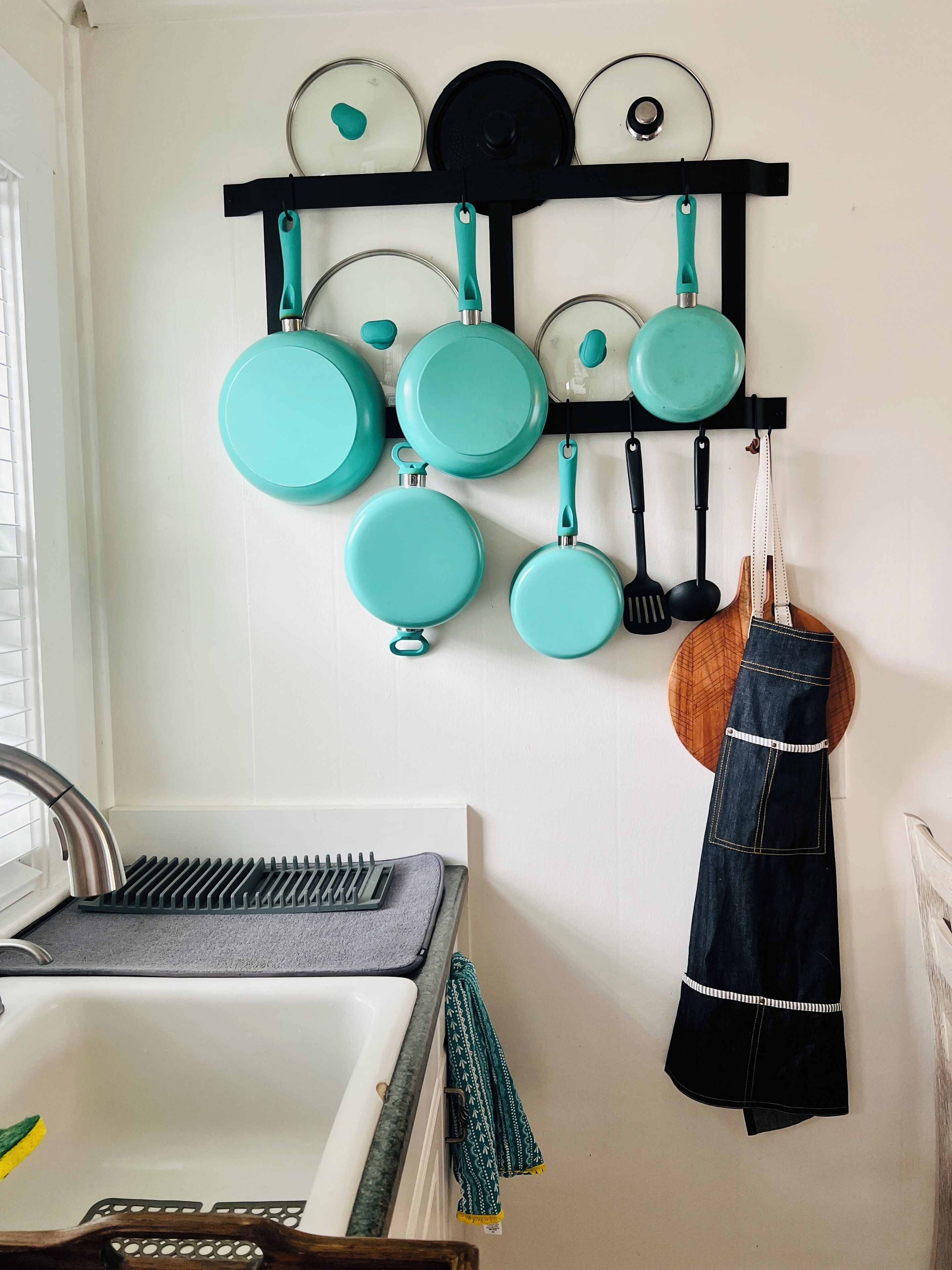 Une cuisine avec un porte-ustensiles fixé au mur, sur lequel sont suspendues différentes casseroles et poêles.