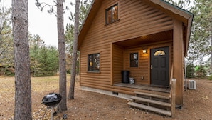 Une cabane en bois avec un porche à l’avant, une porte et un barbecue à l’extérieur.