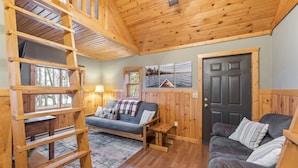 L’intérieur chaleureux d’un chalet comprend un lit en mezzanine, un canapé, une table basse et une porte donnant sur un lac.