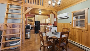 Un intérieur en bois comprenant une table à manger, des chaises, une échelle et un coin cuisine équipé d’appareils électroménagers.