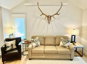 A living room with a sofa, armchairs, and a deer antler mounted on the wall.