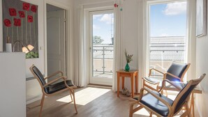 Een lichte kamer met twee grote ramen, een houten vloer en drie stoelen.