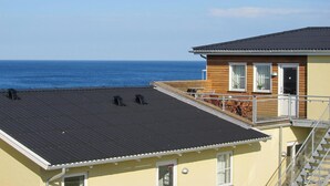Een gebouw met een plat dak met uitzicht op de oceaan, met een klein terras met stoelen en een tafel.