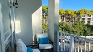 A balcony with a sofa set and a table, a railing, and a view of the street and greenery. - Exceptional Condo on the Bradenton Riverwalk (Bradenton)