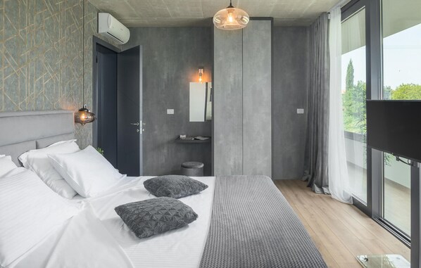 Une chambre moderne avec un grand lit, une table de chevet, un miroir et une vue sur la verdure.