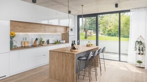 A modern kitchen with a central island, bar stools, and a view of a garden through large windows. - Lovely home in Zminj with sauna (Zminj)