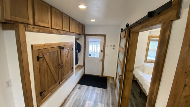 Un couloir avec des armoires en bois, une porte donnant sur une chambre, et un paillasson noir.