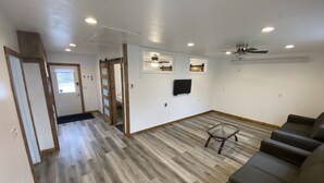 Un vaste salon doté d’un plancher en bois, d’un canapé, d’un téléviseur fixé au mur et d’un ventilateur de plafond.