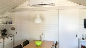 A kitchen with a white ceiling, a white air conditioning unit, a wooden dining table with a green bowl, and a hanging white pendant light. - 2 bedroom cozy home in Nexø (Nexø)