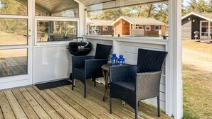 A covered outdoor seating area with wicker chairs and a grill, overlooking a residential area. - 2 bedroom cozy home in Nexø (Nexø)