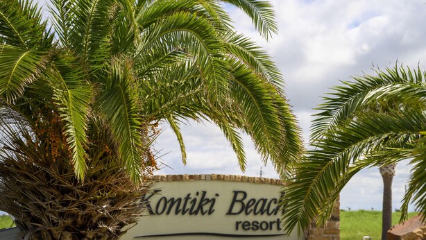 A sign for Kontiki Beach Resort with palm trees in the foreground.