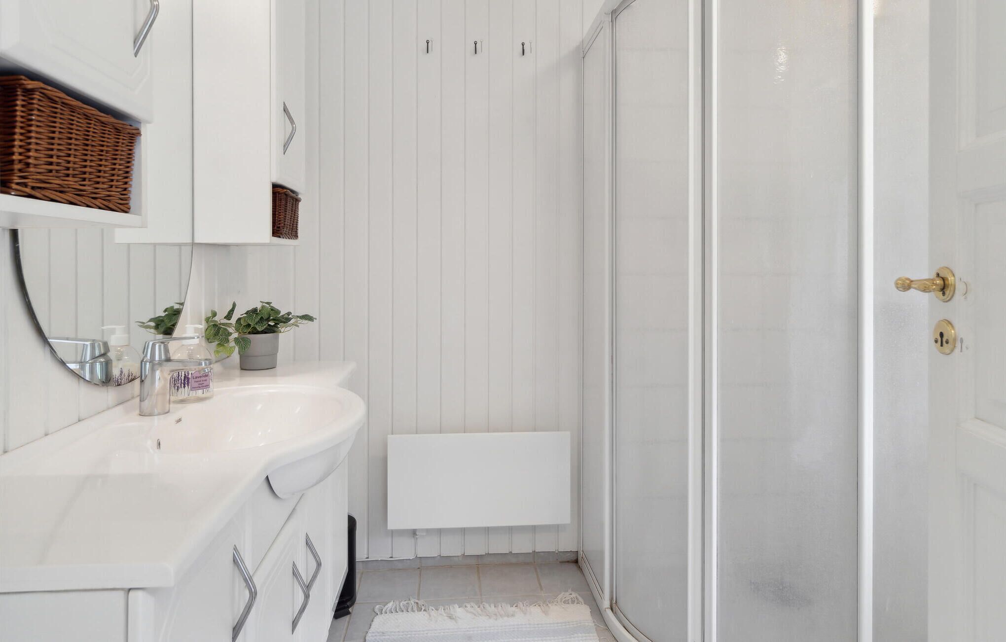 A bathroom with a white sink, a mirror, a potted plant, a shower area, and a radiator.