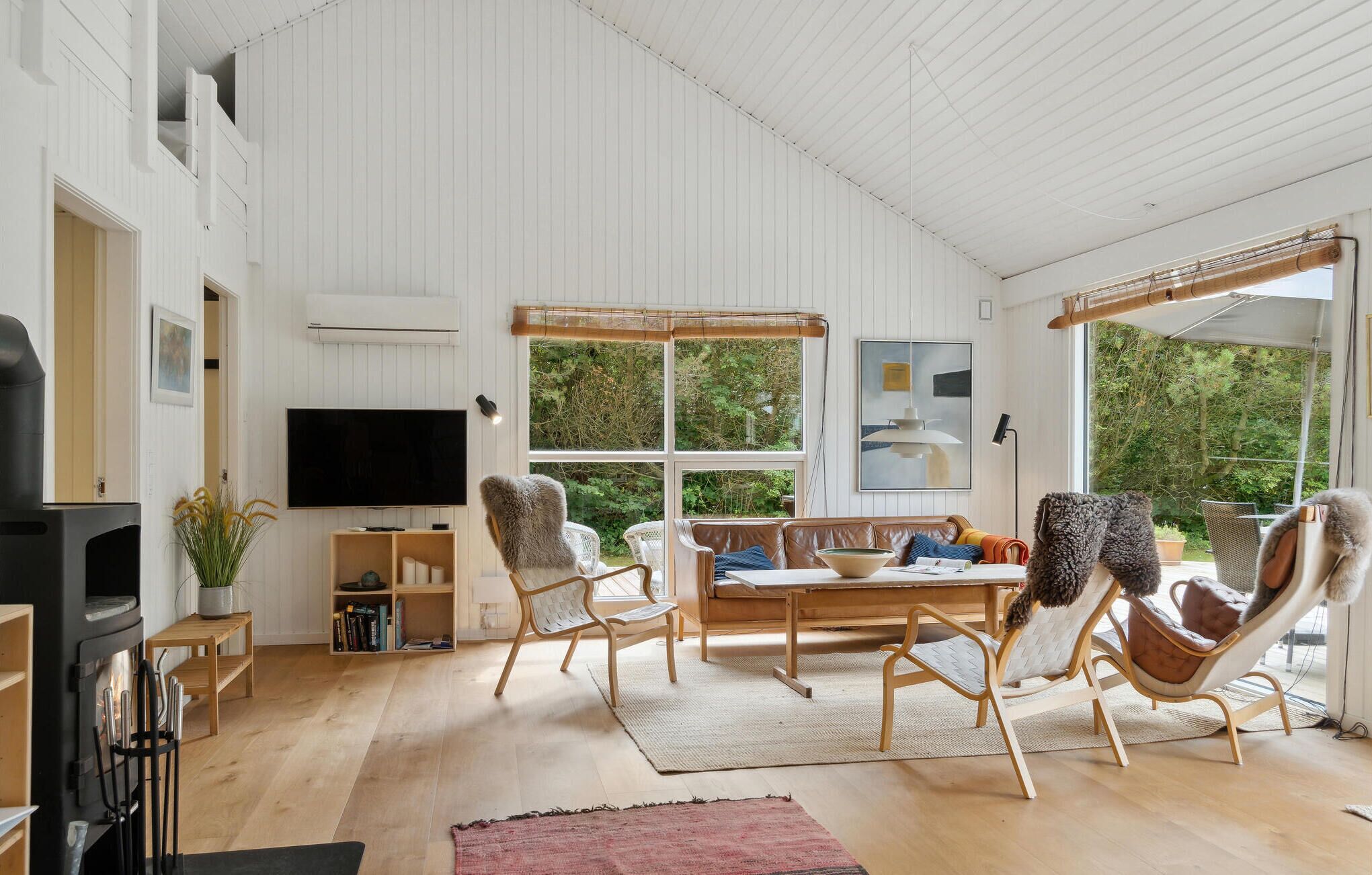 Ein geräumiges Wohnzimmer mit großem Fernseher, Holzboden und einer gemütlichen Sitzecke mit Sofa und Sesseln.