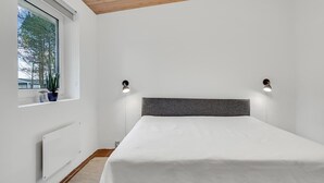 Ein Schlafzimmer mit Bett, weißen Wänden, einem Fenster mit Blick auf Bäume und zwei Wandleuchten.