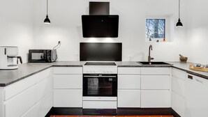 Eine moderne Küche mit weißen Schränken, einem Backofen, einem Kochfeld, einer Mikrowelle und einer Kaffeemaschine.