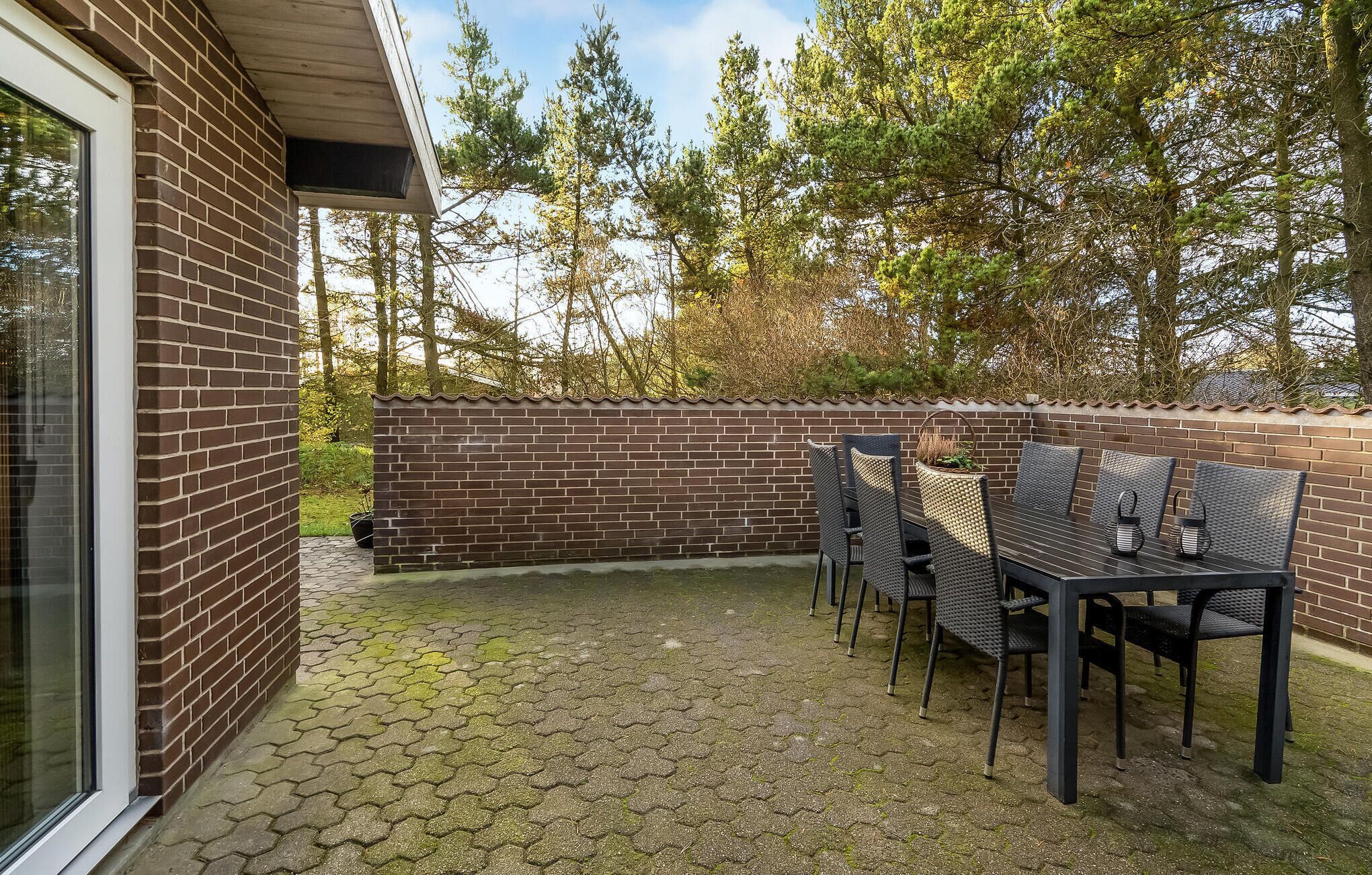 A patio with a brick wall, a table with chairs, and a potted plant.