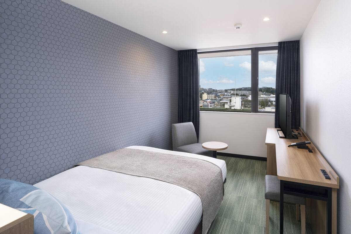 A hotel room with two beds, a desk, a chair, and a view of the city.