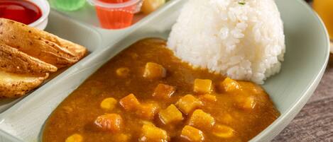 Une assiette de riz, un plat de curry, une portion de pain et un petit bol de sauce.