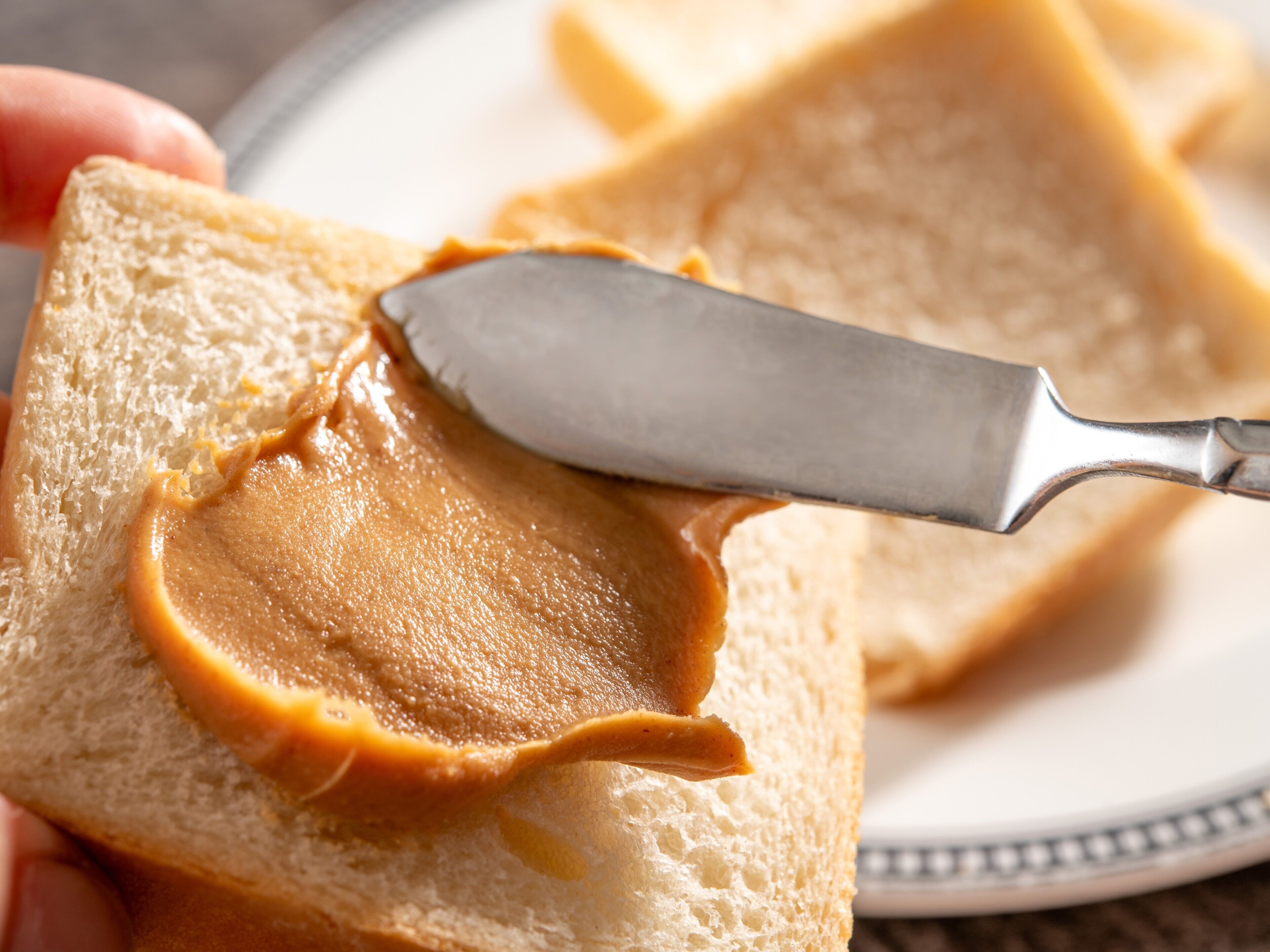Un cuchillo untando mantequilla de maní sobre una rebanada de pan.