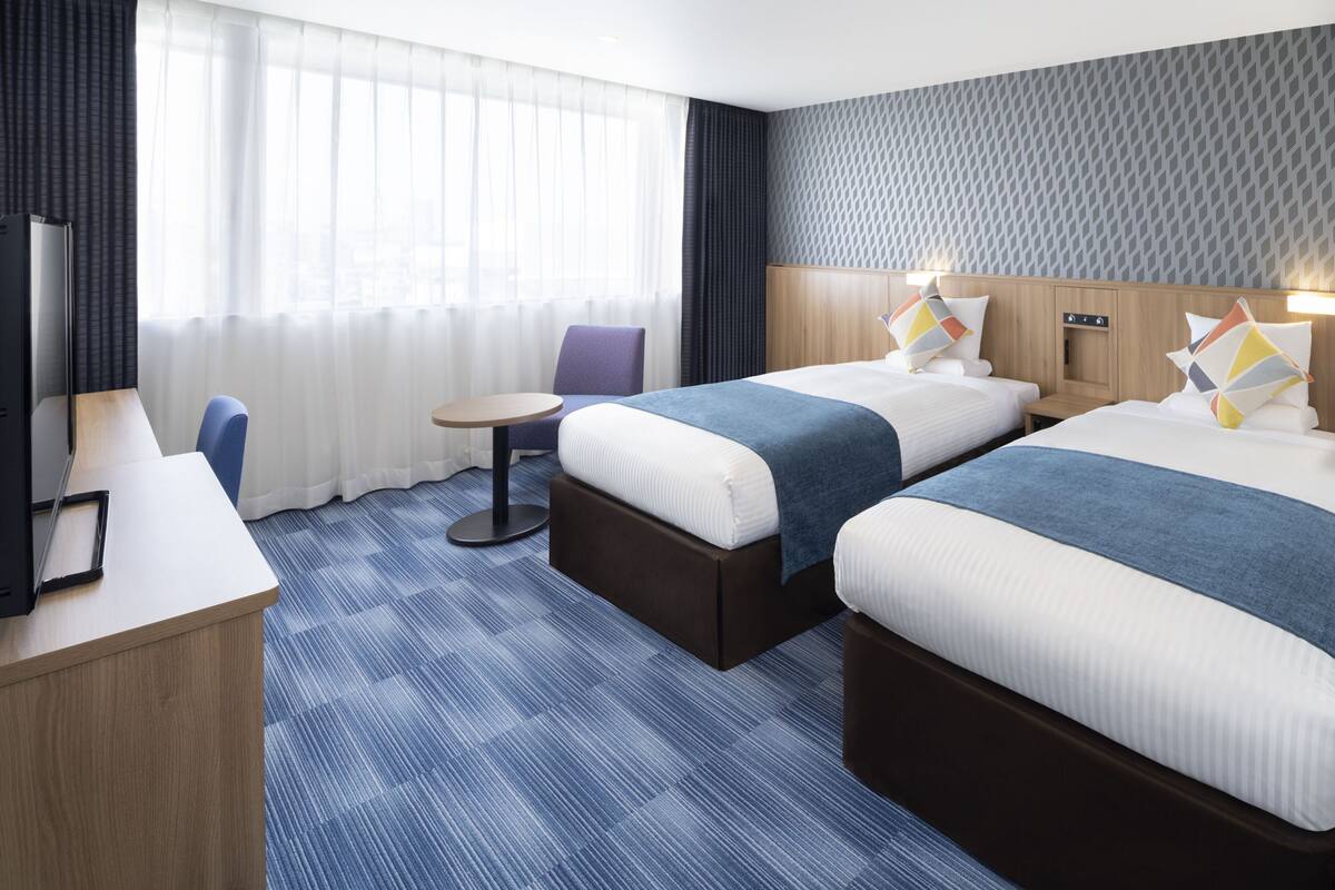 A hotel room with two beds, a desk, a chair, and a small table.