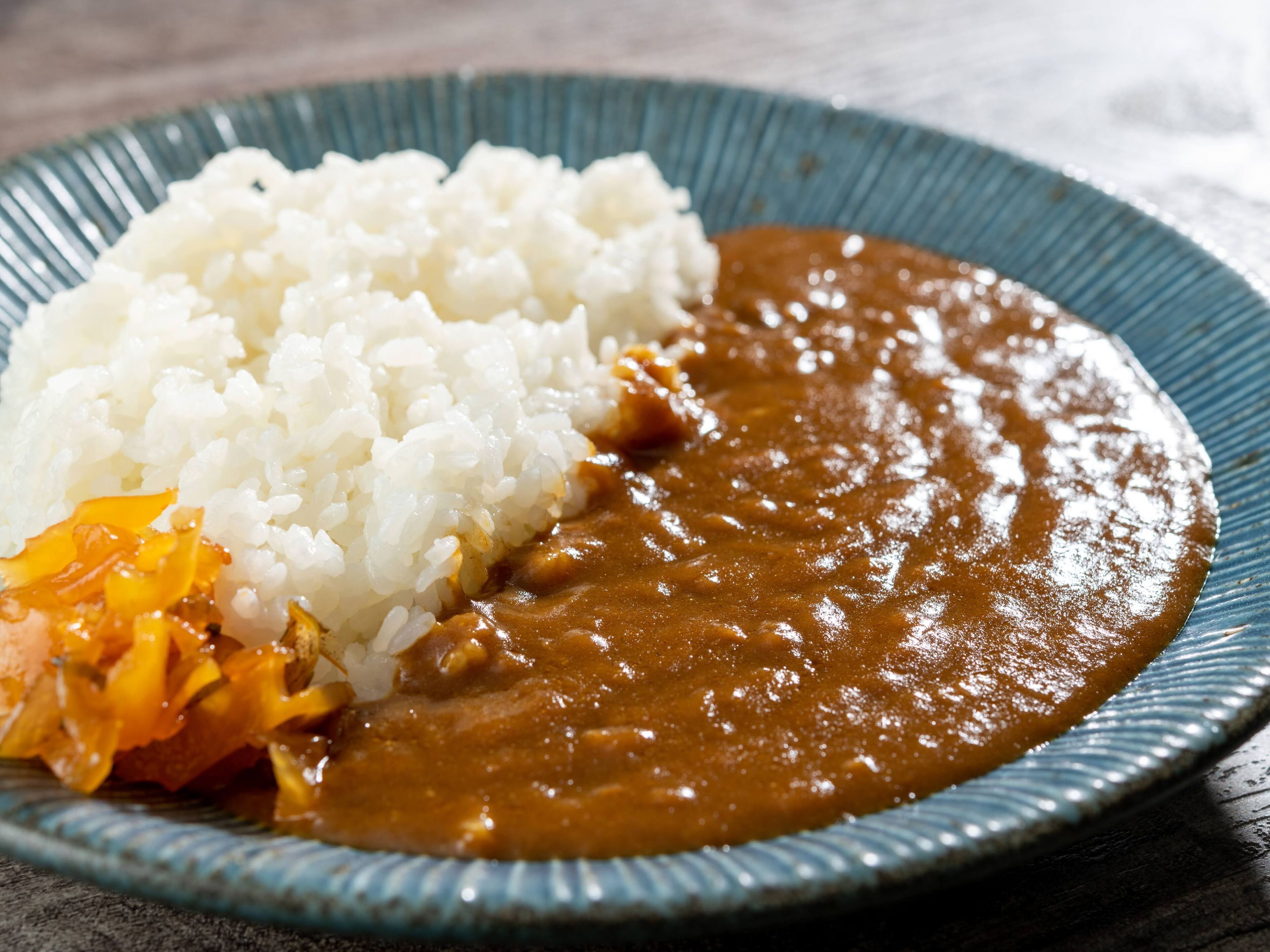 Une assiette de riz blanc et une sauce brune, accompagnée d’un morceau de légume orange.