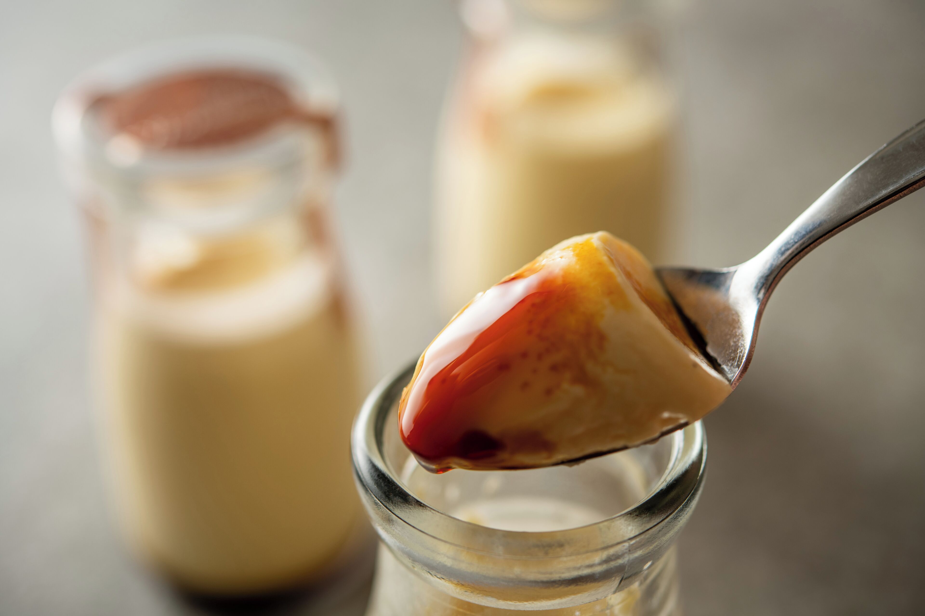 Una cucharada de postre cremoso con cobertura brillante, sostenida sobre un vaso transparente.