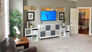 A living room with a flat-screen TV mounted on the wall, a white entertainment unit with patterned storage, a potted plant, and a door leading to a balcony.