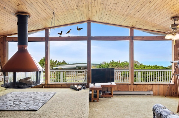 A wooden cabin with a large window, a fireplace, a TV, and a view of the landscape.