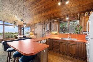 A wooden cabin kitchen with a large island, bar stools, and a view through the windows.