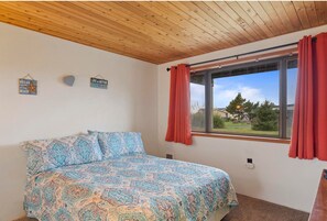 A bedroom with a bed, wooden ceiling, window with red curtains, and two wall decorations.