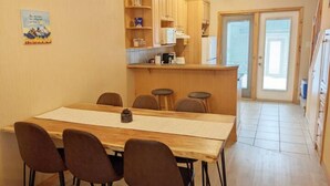 Un comedor con mesa y sillas de madera, una cocina con armarios de madera, y una puerta que da a otra habitación.