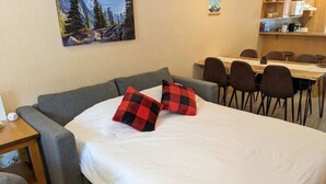 Una habitación con cama, sofá gris y zona de comedor con sillas y mesa.