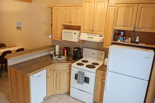 A compact kitchen with wooden cabinets, a microwave, a stove, a dishwasher, and a refrigerator.