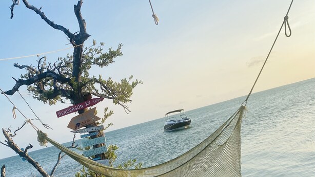 A hammock strung between trees, a boat on the water, and a sandy beach. - Luxury and Lovely Water Front House (Big Pine Key)