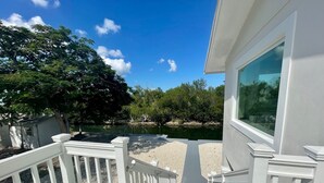 A wooden deck with white railings, a clear view of a lake, and a building with a large window. - Luxury and Lovely Water Front House (Big Pine Key)