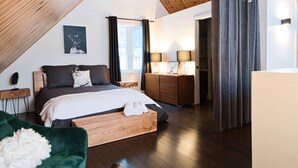 Une chambre avec un plafond en pente, un lit doté d’une tête de lit en bois, une table de chevet, une commode et une fenêtre avec des rideaux.