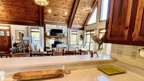 A spacious kitchen with a large island, wooden beams, and a stone fireplace.