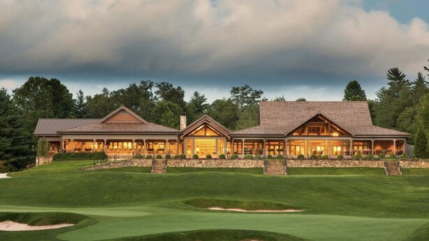 A large, two-story house with a stone facade and multiple windows, surrounded by a well-maintained lawn and a golf course.