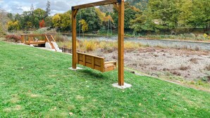 Een houten schommel en een bank in een park, met een rivier en herfstbomen op de achtergrond.