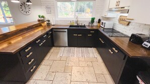 Een moderne keuken met een centraal eiland, zwarte kastjes, een vaatwasser van roestvrij staal en een raam dat zorgt voor daglicht.