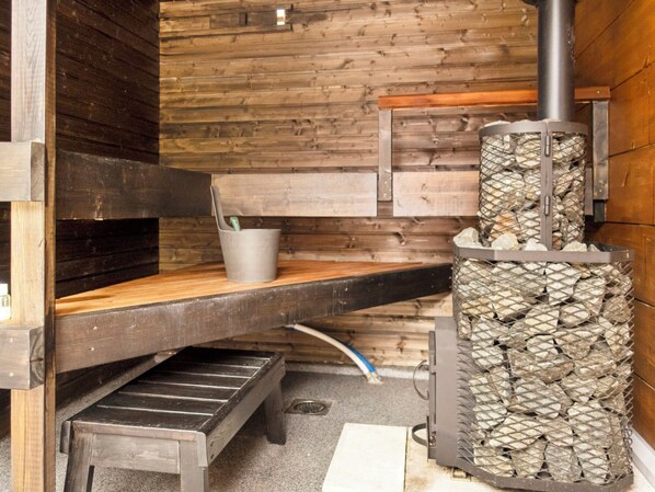 A rustic wooden interior with a built-in wood stove, a bench, and a small table. - Solokoto by Interhome (Inari)