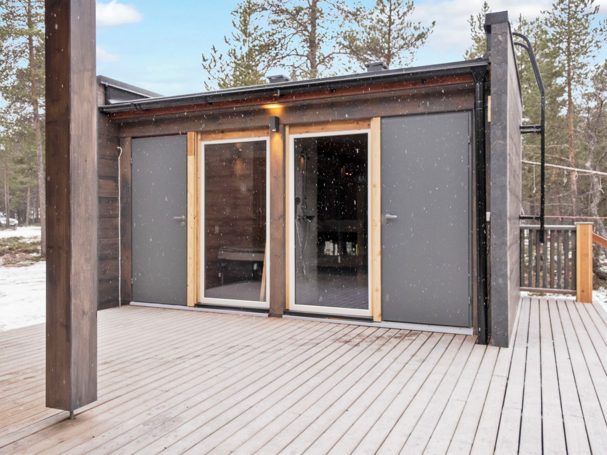 A wooden deck with a modern building featuring large glass doors and a metal railing.