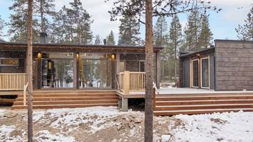 A cabin with a wooden deck and glass doors, surrounded by snow and trees.