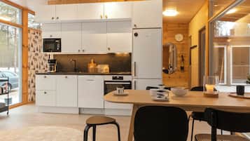 A modern kitchen with white cabinets, a microwave, and a stove. There is a dining table with chairs and a candle on it.