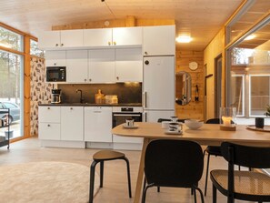 A modern kitchen with white cabinets, a microwave, and a stove. There is a dining table with chairs and a candle on it. - Solokoto by Interhome (Inari)