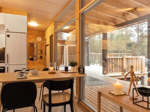 A modern kitchen with a wooden interior, a dining area with chairs, a table with a candle, and a view of the outdoors. - Solokoto by Interhome (Inari)