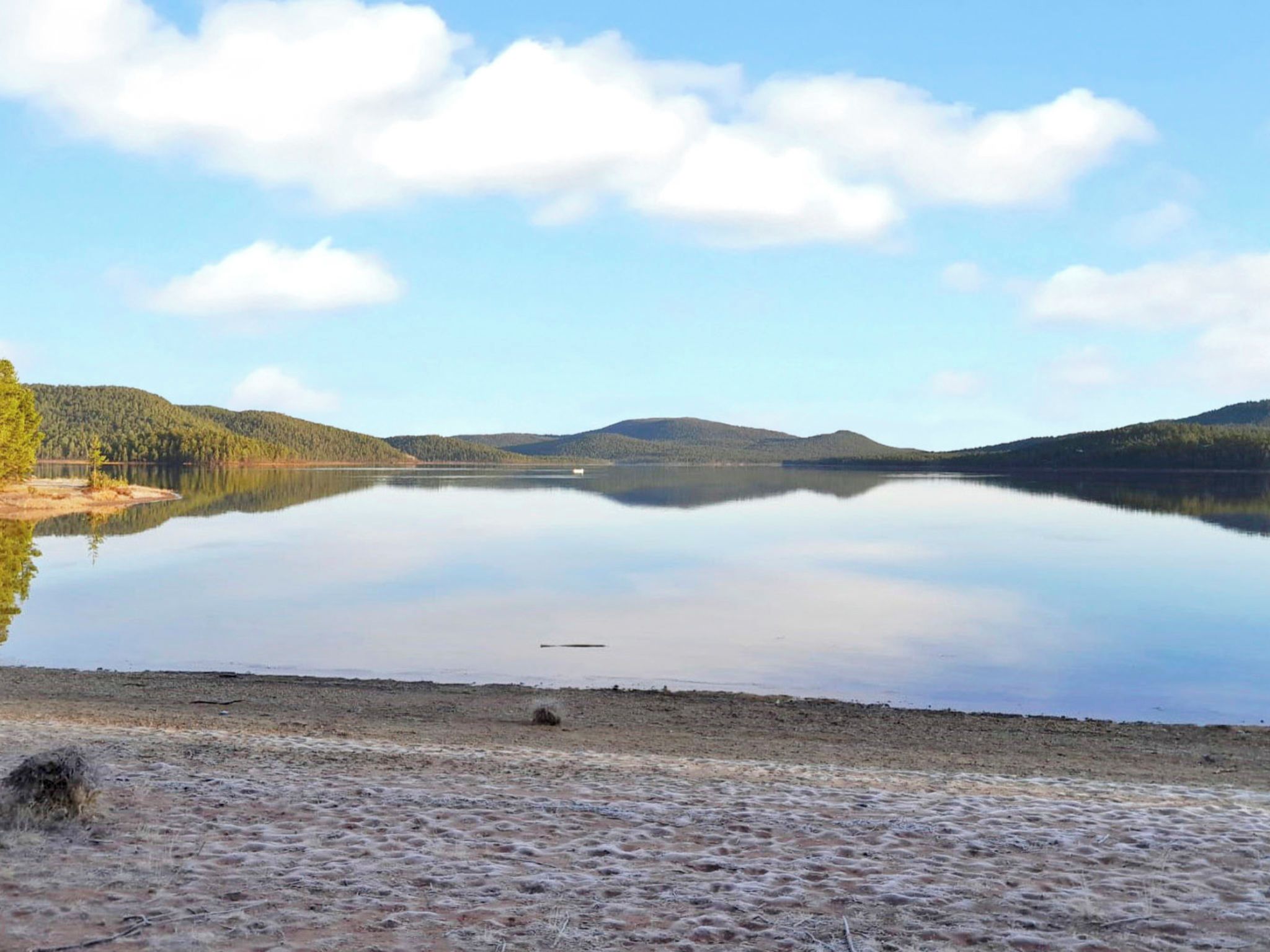 Un lago tranquilo con cielo despejado y colinas boscosas al fondo.